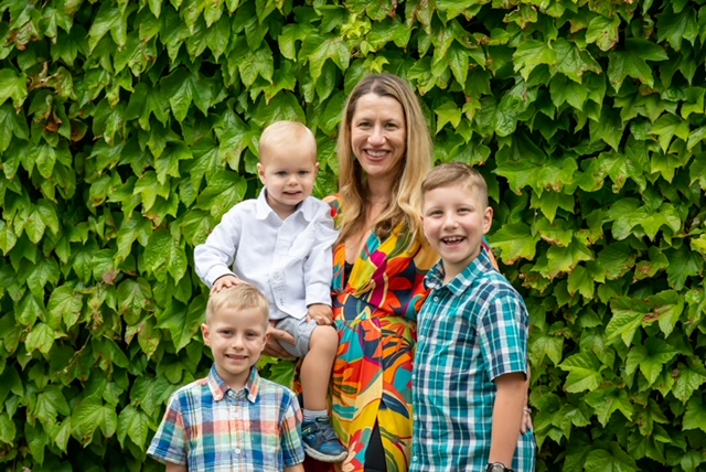 A photo of Dr. Anne Slater standing with her three children in front of green vegetation. 