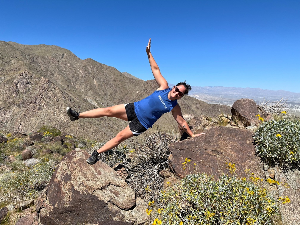 Dr. Terri Laguna does a side plank on a hike, wearing a blue shirt and black shorts. 