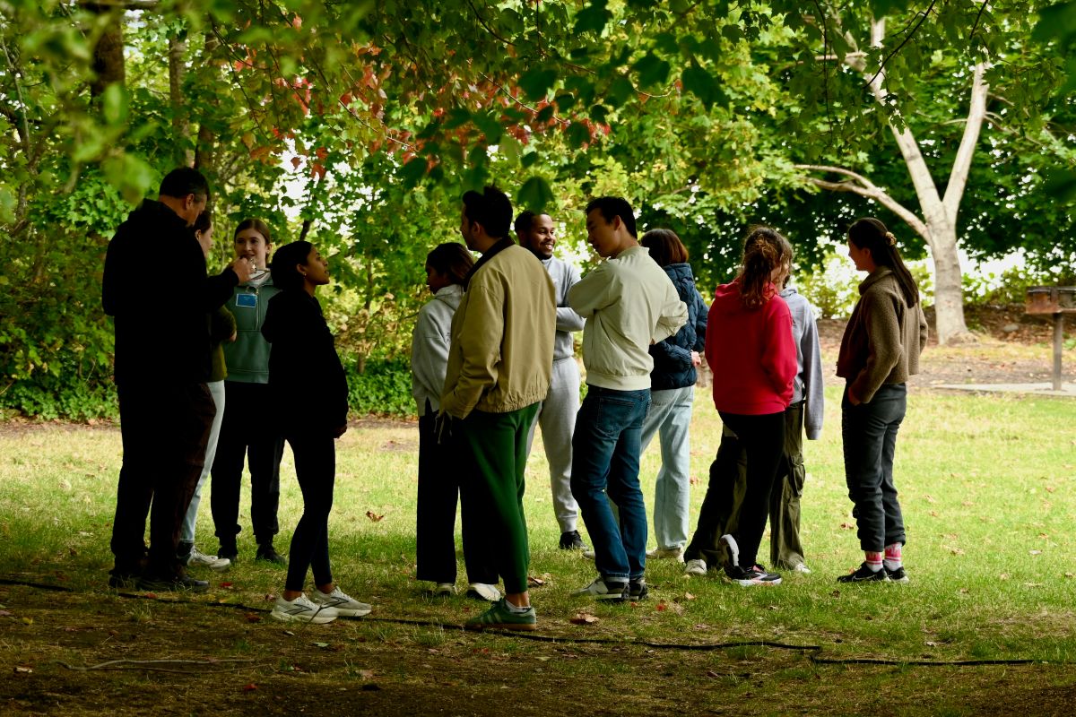 A group of people stand outside in a wooded area. 