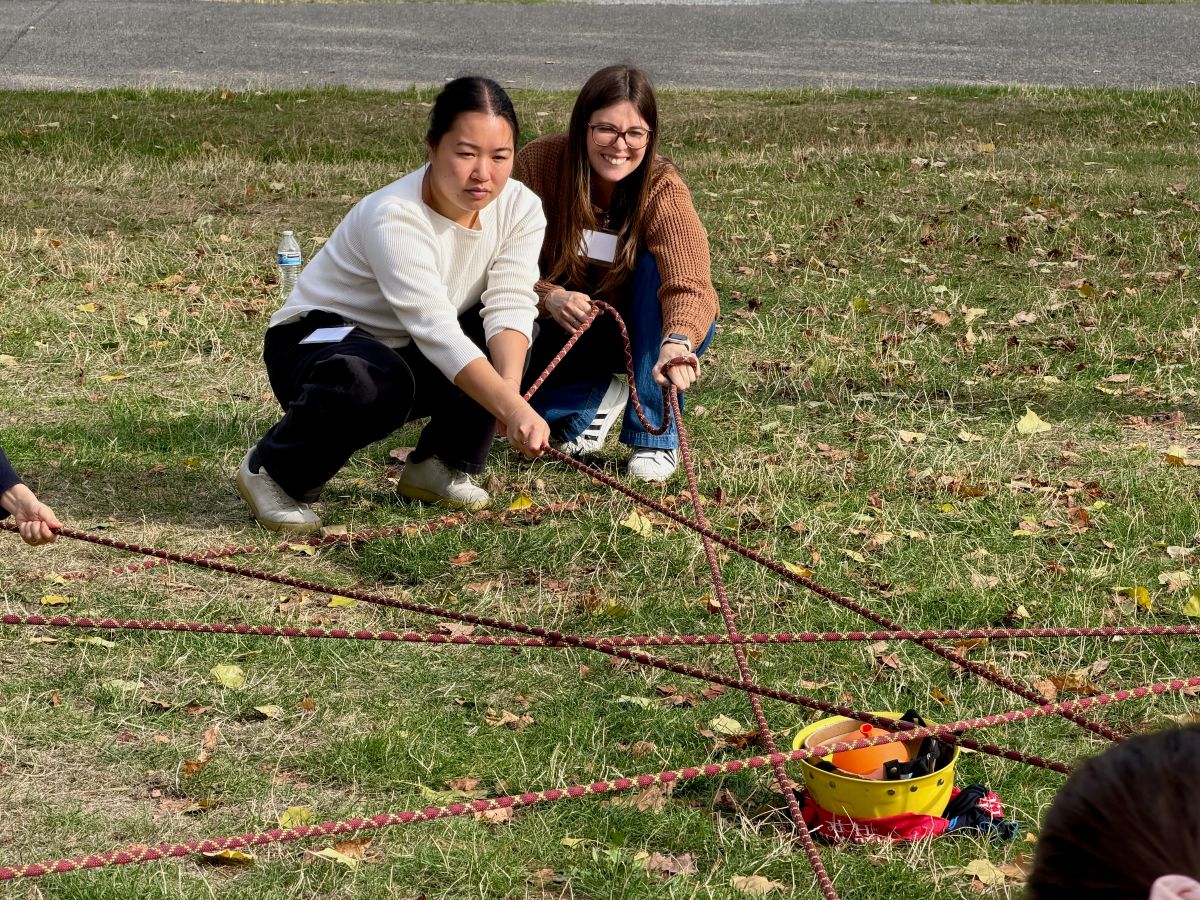 Two people crouch on the grass holding a rope as they participate in a team building activity.