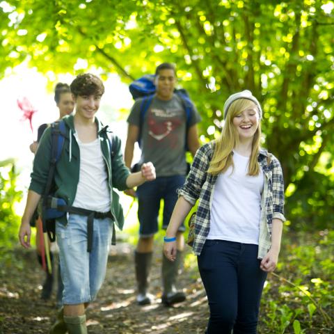 Four teenagers smiling as they walk on a hiking trail.