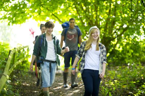 Four teenagers smiling as they walk on a hiking trail.